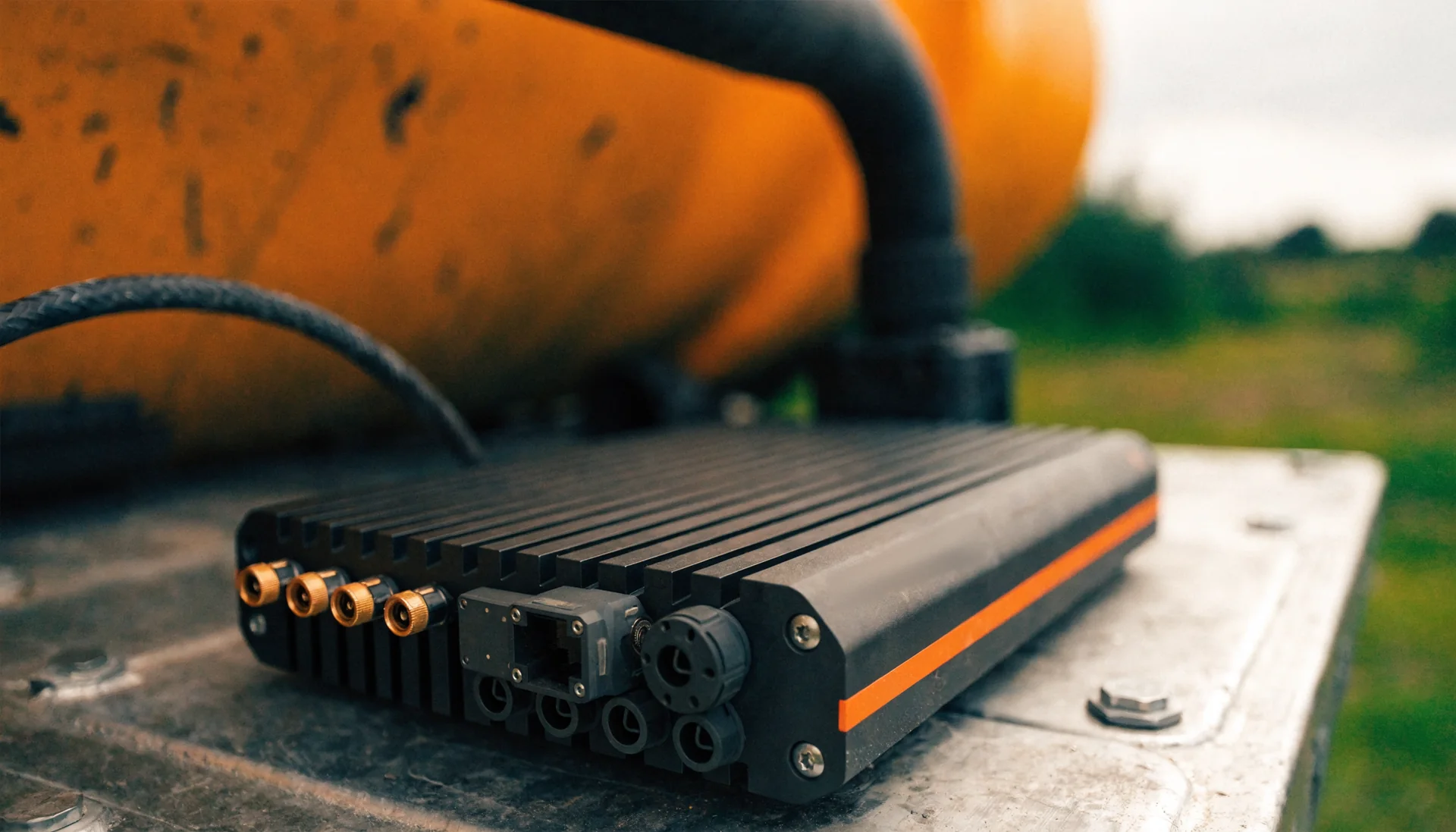 Render: HP-FN1 Micro, a finned black aluminium unit with an orange stripe and its connectors at one end, on the deck of a vehicle.